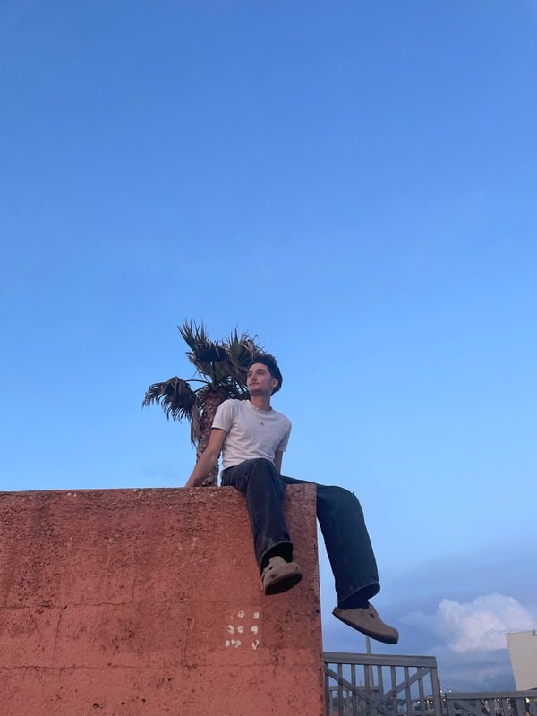 William, assis sur un mur sous un ciel bleu
